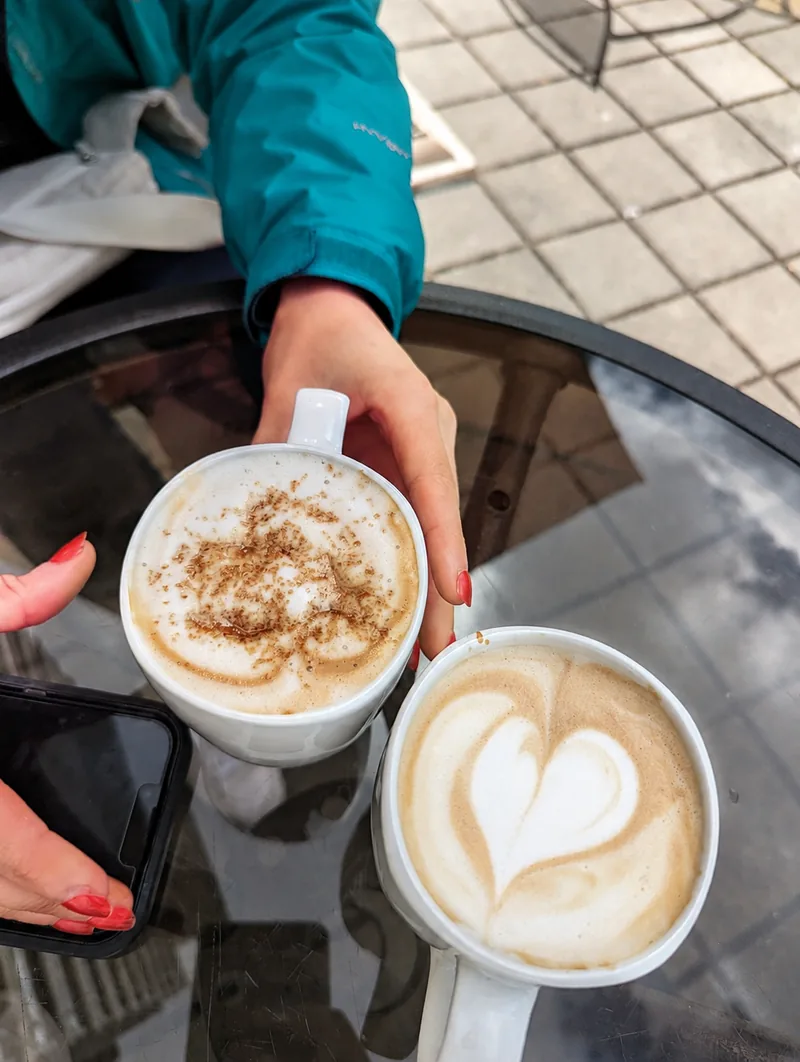 Two coffees with latte art held over a café patio table